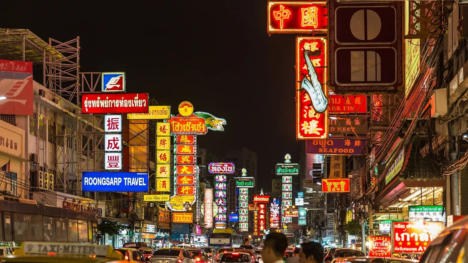 Neon shop signs above traffic on Yaowarat Road in Chinatown at night