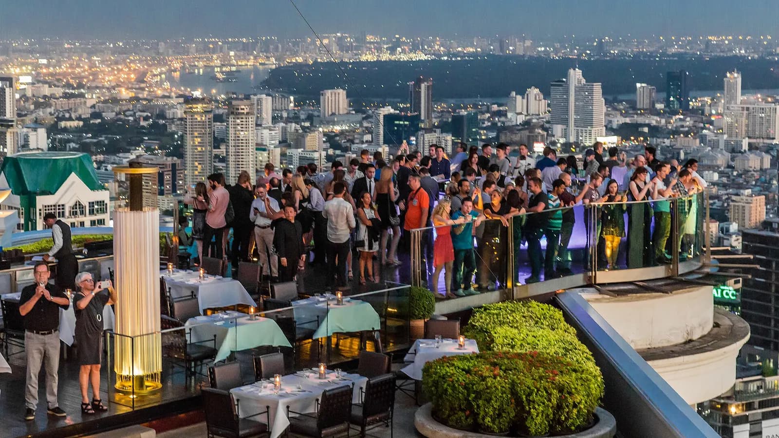 Guests at Sky Bar on top of lebua at State Tower looking over the Chao Phraya River at dusk