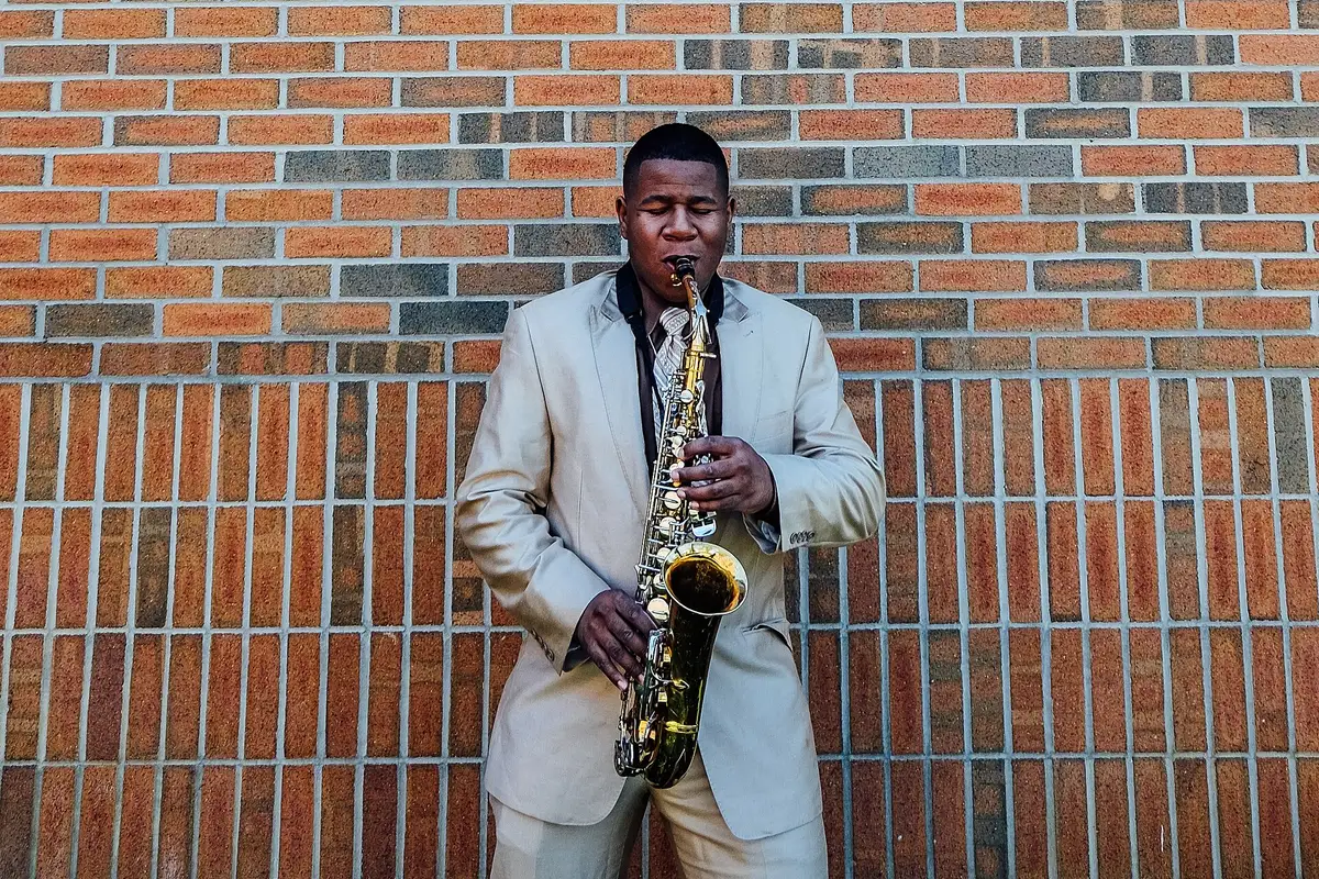 A saxophonist playing in front of a brick wall